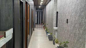 A corridor with a tiled floor, potted plants, and a wooden door on the left. - Hotel Natraj A Boutique Hotel (Haridwar)