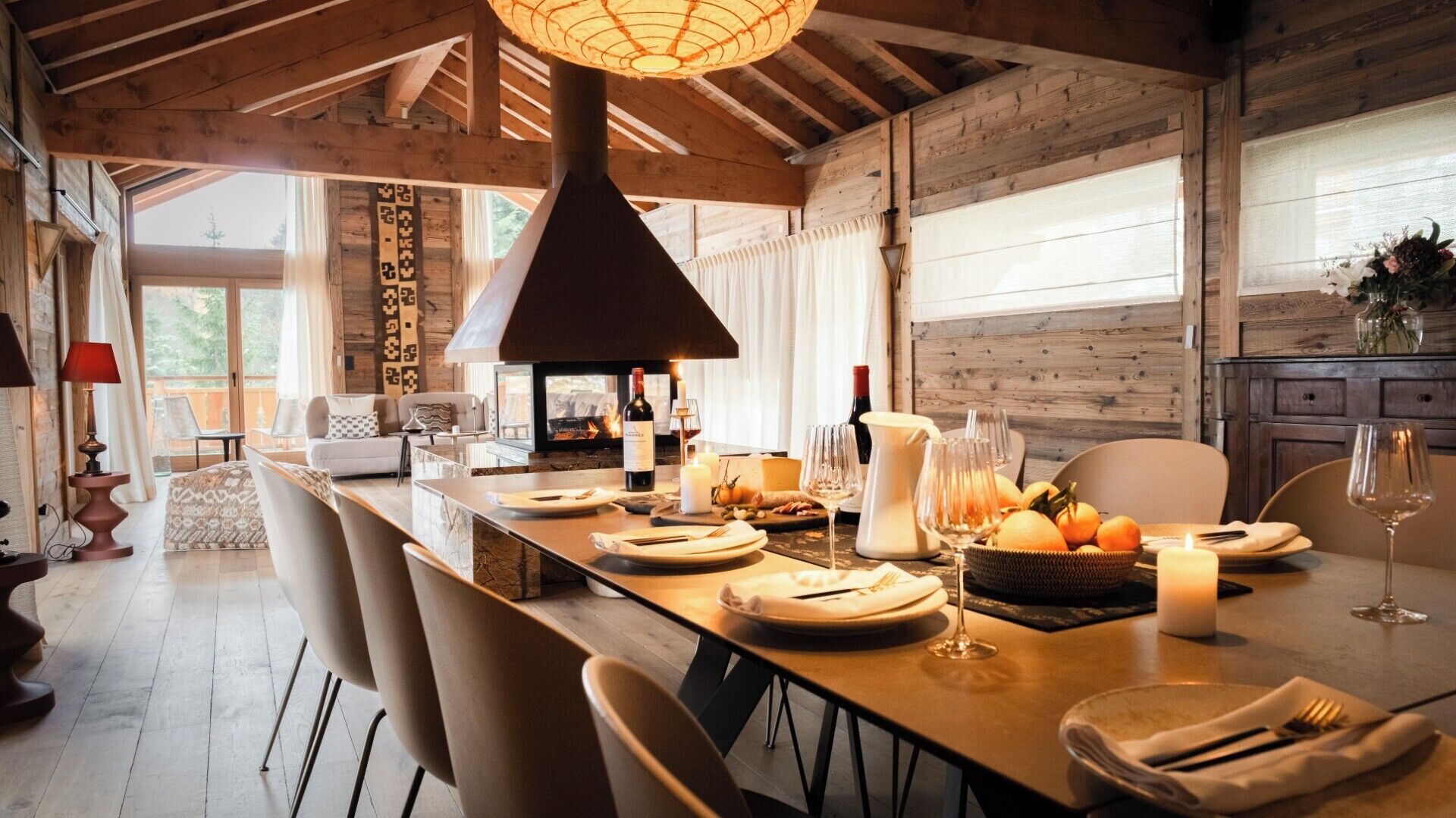 A dining area with a long table set for a meal, a fireplace, and a view of the outdoors.