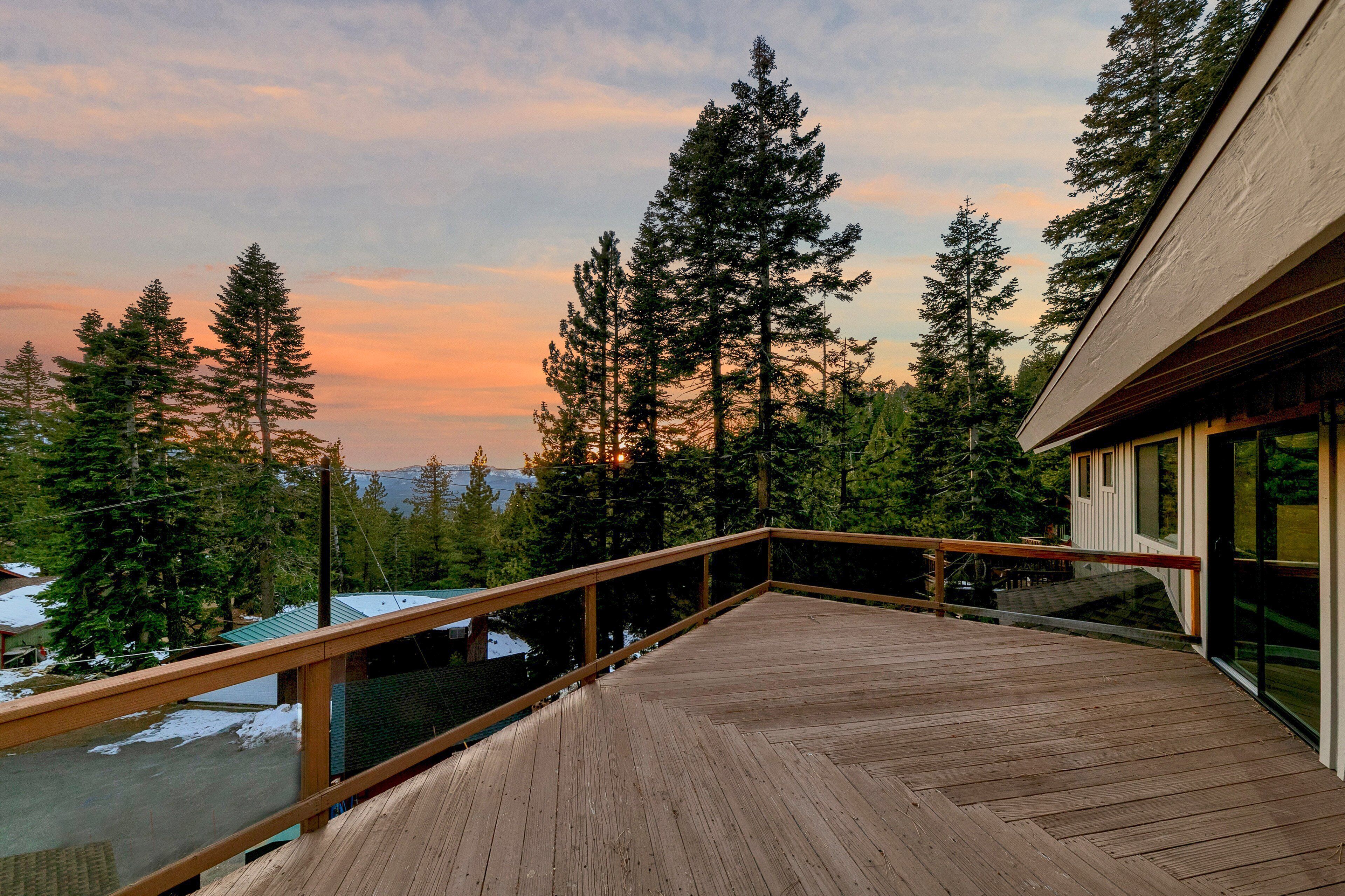 A wooden deck with a railing overlooking a forested area and a building with large windows.