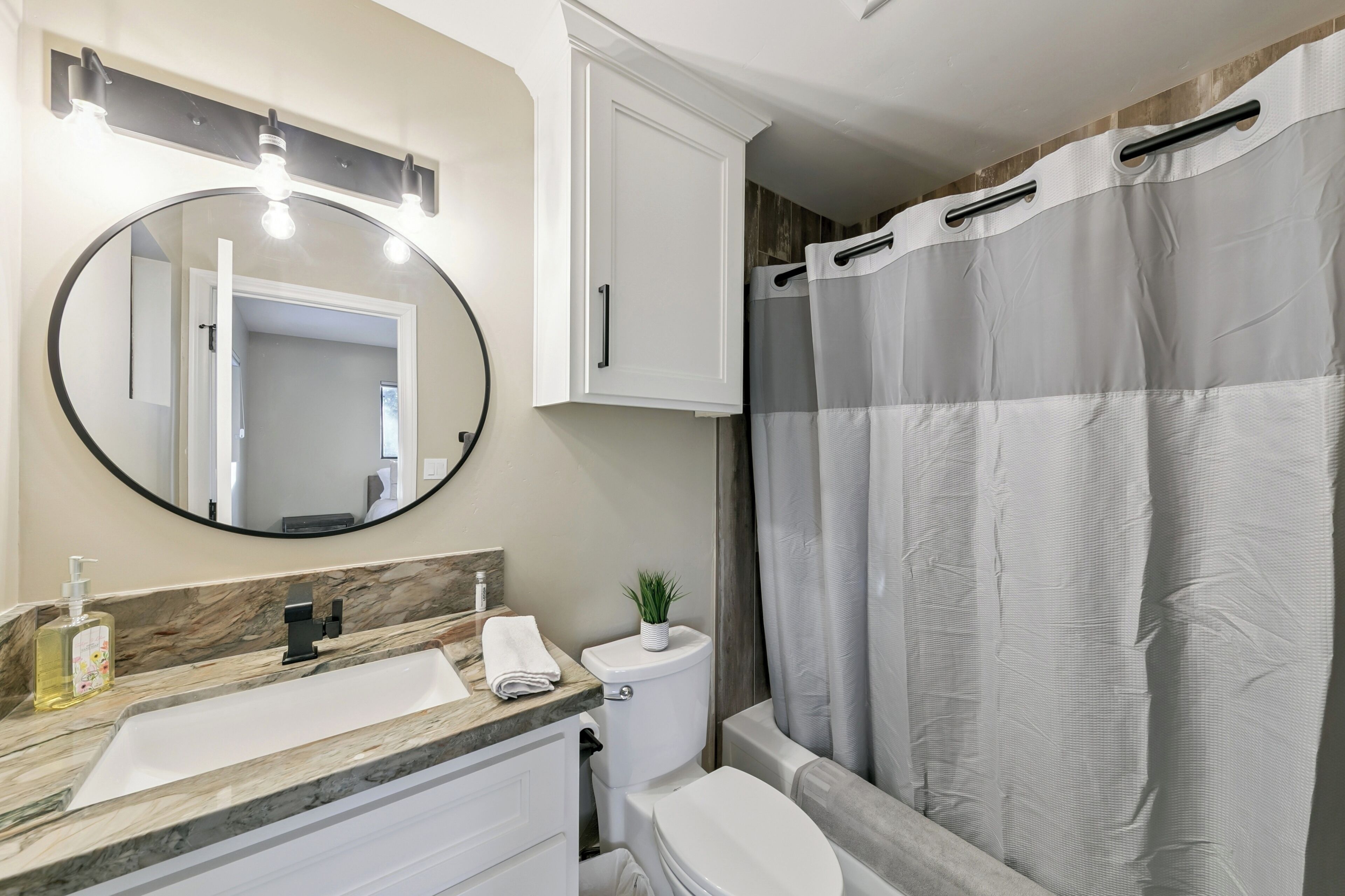 A bathroom with a sink, mirror, toilet, and shower curtain.