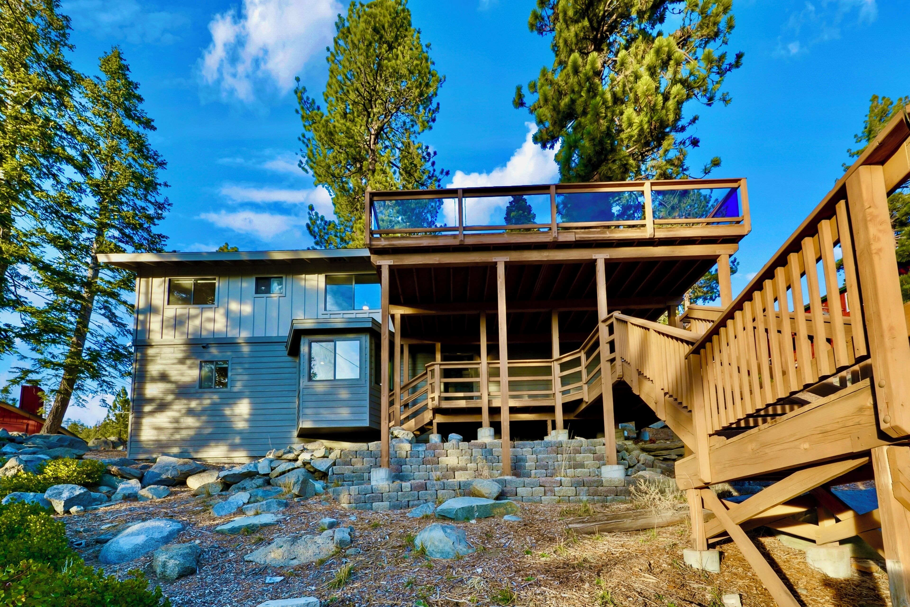A modern cabin with a wooden deck and stairs leading to a second-story balcony.