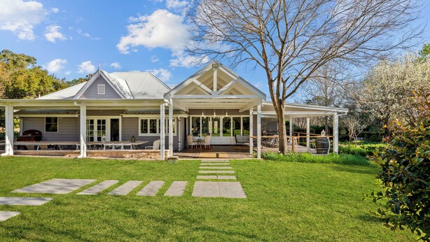 A large, two-story house with a covered patio area, a lawn, and a stone pathway leading to the entrance.