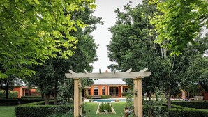 A garden with a pergola, a swimming pool, and a building in the background.