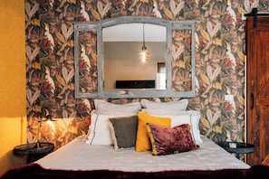 A bedroom with a bed, pillows, a mirror, and a wall with a floral pattern. - One Bedroom Studio with a Shared Pool (Arcadia)
