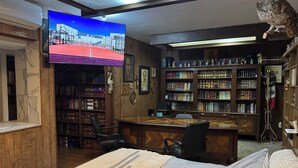 Ein Arbeitsraum mit großem Fernseher, Bücherregalen, einem Schreibtisch und einer gemütlichen Sitzecke.