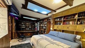 Ein gemütliches Schlafzimmer mit einem großen Bett, einem Schreibtisch und einem Bücherregal voller Bücher.