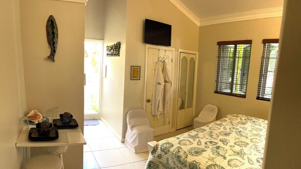 A bedroom with a bed, a desk with a chair, and a bathroom with a shower and a toilet. - Tropical King Studio Apartment (Nassau)