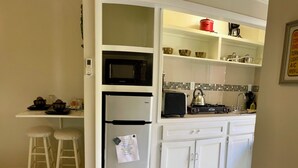 A kitchen with white cabinets, a microwave, a refrigerator, and a stove. There are stools and a small table with cups and a kettle. - Tropical King Studio Apartment (Nassau)