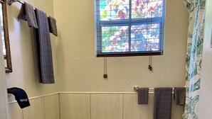 A small, clean bathroom with a toilet, sink, and window. - Tropical King Studio Apartment (Nassau)