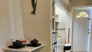 A compact kitchen with a dining area, a white door, and a small stool. - Tropical King Studio Apartment (Nassau)
