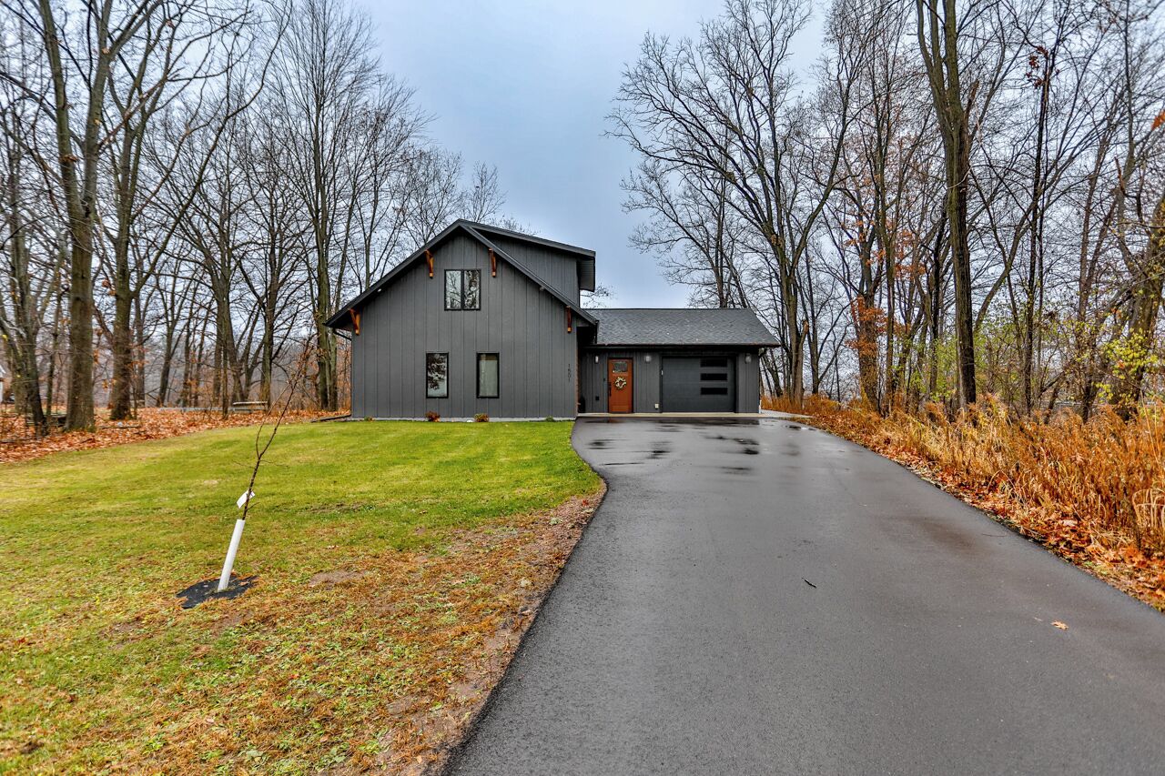 A two-story house with a grey exterior, a front porch, and a driveway leading to the garage.