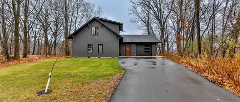 A two-story house with a grey exterior, a front porch, and a driveway leading to the garage.