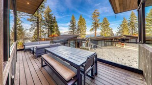 Una terrazza in legno con panchina e tavolo, affacciata su un paesaggio montuoso con alberi.