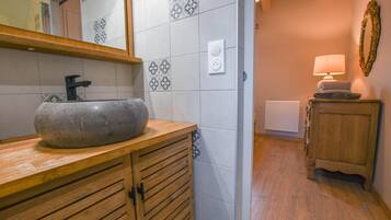 Ein Badezimmer mit Holzwaschtisch, Steinwaschbecken, Spiegel, einer Leuchte und einem Handtuchhalter.