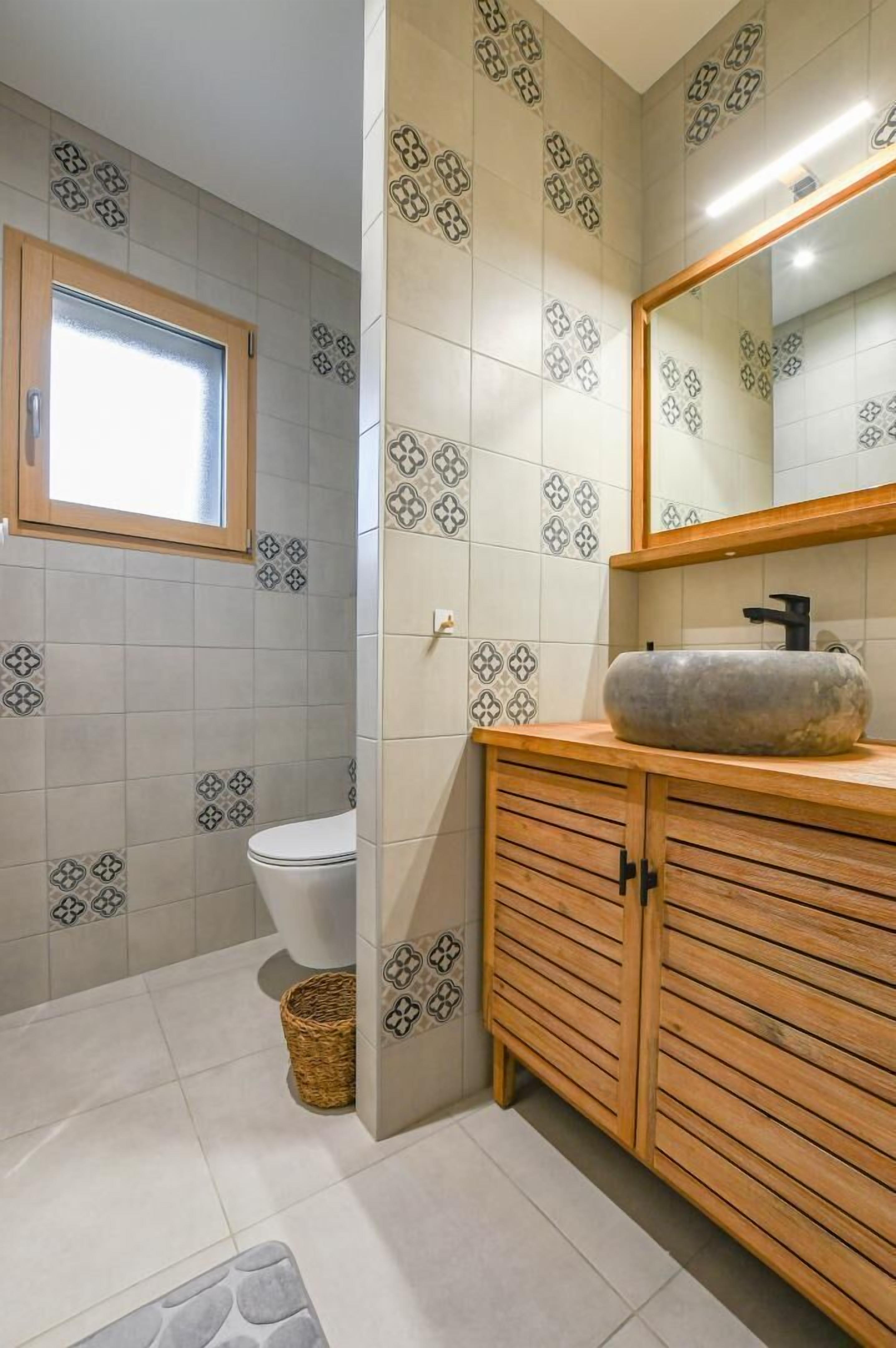 Et badeværelse med mønstret flisegulv, et trækommode, en vask og et toilet.