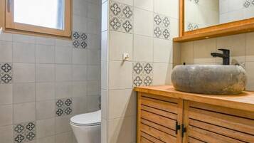 Et badeværelse med mønstret flisegulv, et trækommode, en vask og et toilet.