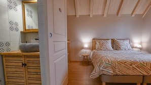 A bedroom with a bed, bedside lamps, a wooden nightstand, and a bathroom with a sink and mirror. - La Ferm'Hier - BALNOT SUR LAIGNES (BALNOT SUR LAIGNES)