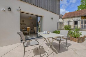 An outdoor patio with a table and chairs, a door leading to an interior dining area, and a small garden with plants. - La Ferm'Hier - BALNOT SUR LAIGNES (BALNOT SUR LAIGNES)