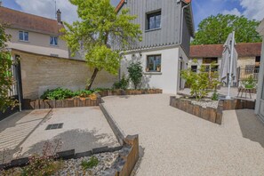 Un patio con zona de grava, macetas de madera y un edificio de fachada gris y tejado de tejas rojas.