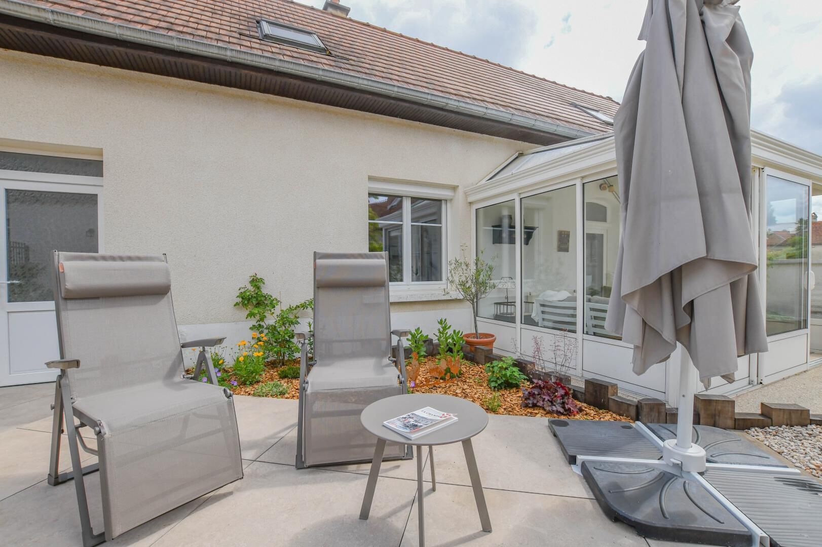 Eine Terrasse mit zwei Loungestühlen, einem kleinen Tisch und einem überdachten Bereich mit Sonnenschirm.