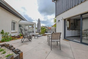 A patio with outdoor furniture, a glass door leading to a kitchen, and a garden area with plants.