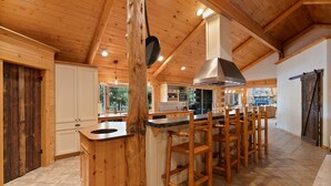 A spacious kitchen with wooden cabinets, a central island with bar stools, and a large stove. - Risa Cabin: Full Lodge | Lake, Hot Tub, 9 Acres (Bend)