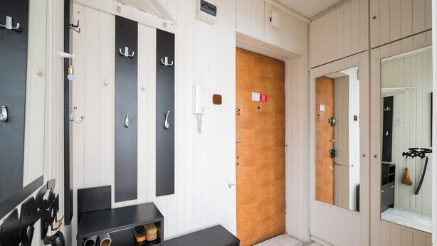 A hotel room with a wooden door, a black and white wardrobe, a small desk with a telephone, and a mirror. - Mokotów Urban Comfort Apartment (Warszawa)