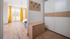 A modern room with a wooden floor, a small wooden bench, a white wardrobe, and a wall-mounted coat rack. - Bemowo Lotnisko Snug Apartment (Warszawa)