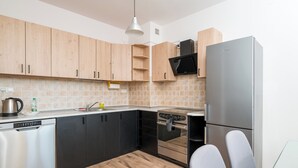 A modern kitchen with wooden cabinets, a stainless steel dishwasher, a built-in oven, and a refrigerator. - Bemowo Lotnisko Snug Apartment (Warszawa)