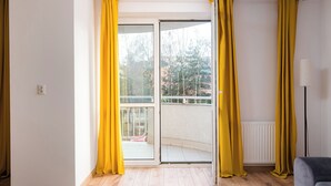 A room with a sliding glass door leading to a balcony, a floor lamp, and a wooden floor. - Bemowo Lotnisko Snug Apartment (Warszawa)