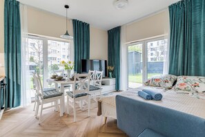 A modern bedroom with a bed, a TV, and a dining area with chairs and a table. - Gdynia Marina Apartment with Garden (Gdynia)