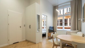 A modern apartment with a dining area, a TV, and a view of buildings through large windows. - Dyrekcyjna Charming Apartment (Katowice)