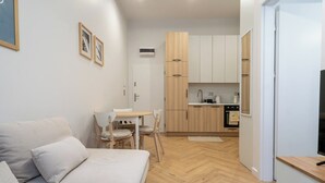 A modern living room with a sofa and chairs, a small dining table, and a kitchen area with wooden cabinets and appliances. - Dyrekcyjna Charming Apartment (Katowice)