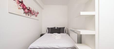 A modern bedroom with a bed, a nightstand, a radiator, and a wall-mounted shelf.
