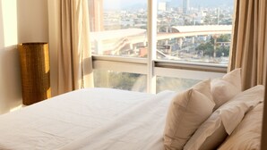 Une chambre d’hôtel avec un grand lit, des rideaux de couleur beige et une vue sur le paysage urbain, visible à travers de grandes fenêtres.