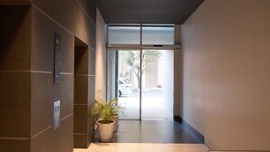 Un couloir moderne avec une porte en verre donnant sur un espace de stationnement. Des plantes en pot sont disposées le long du mur.