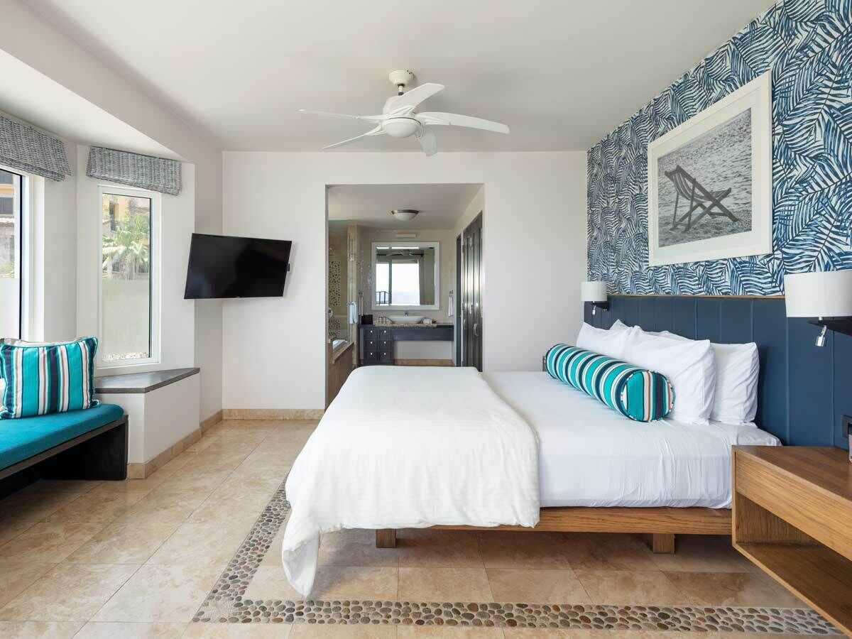 Quarto com cama, televisão, um banquinho e parede estampada.