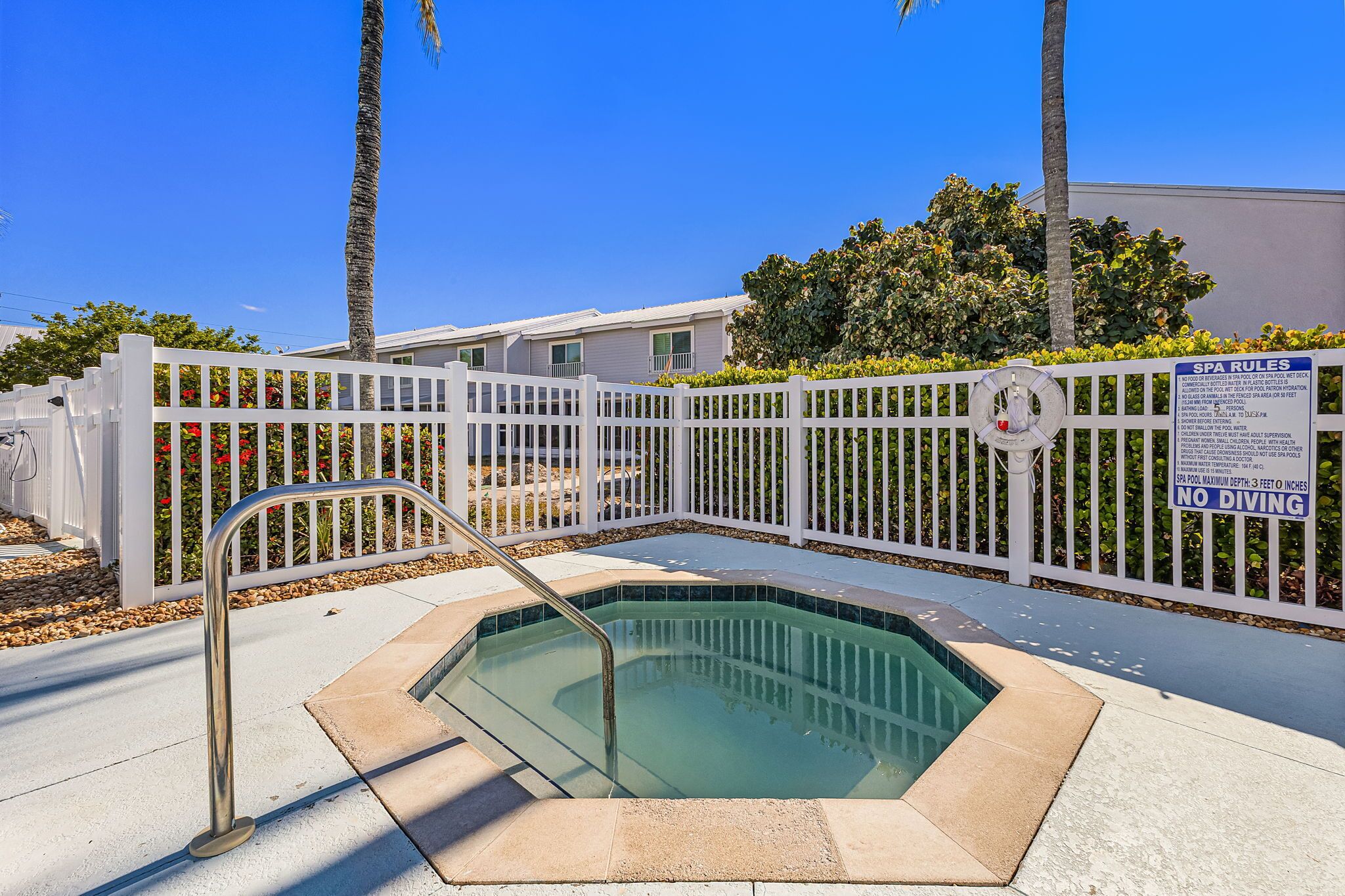 A pool area with a white fence, a lifeguard chair, and a sign indicating no diving.