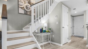 Un escalier avec des rampes blanches menant à un palier où se trouvent une table en verre et une lampe.