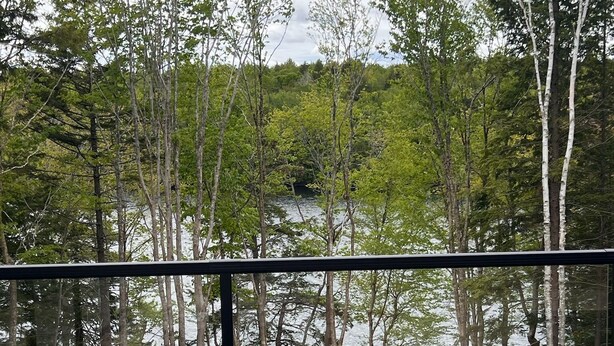 Une terrasse en bois avec deux chaises en bois, donnant sur un barbecue et un lac entouré d’arbres.