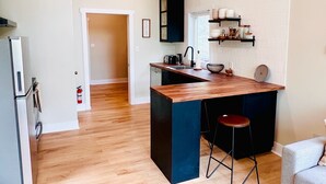 Une cuisine moderne avec un îlot central en bois, des tabourets de bar noirs et un four encastré.