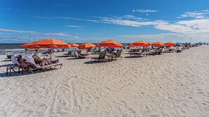 En strand med rader av solstolar och orangefärgade parasoller.