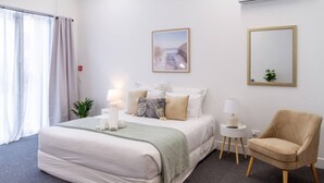 Une chambre d’hôtel bien rangée, avec un grand lit, une chaise, une petite table et un tableau accroché au mur.