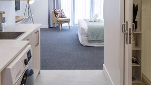 Une chambre d’hôtel moderne équipée d’une kitchenette, d’un lit, d’une chaise et offrant une vue sur l’extérieur.