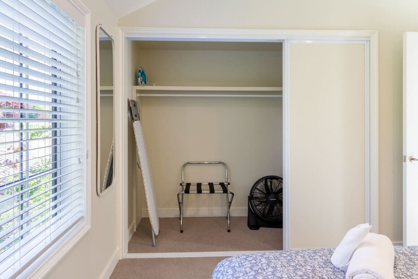 Ein Schlafzimmer mit Bett, Schrank, Wäscheständer und Ventilator.