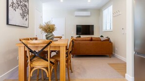A modern living room with a wooden dining table and chairs, a sofa, a flat-screen TV, and a decorative vase.