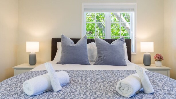 A neatly made bed with a floral-patterned bedspread, two pillows, and two rolled towels on the side.