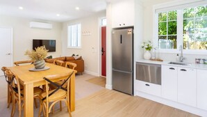 A modern kitchen with white cabinetry, a stainless steel refrigerator, and a dining area with a wooden table and chairs.