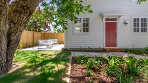 A white house with a red door, a wooden fence, and a tree in the foreground.