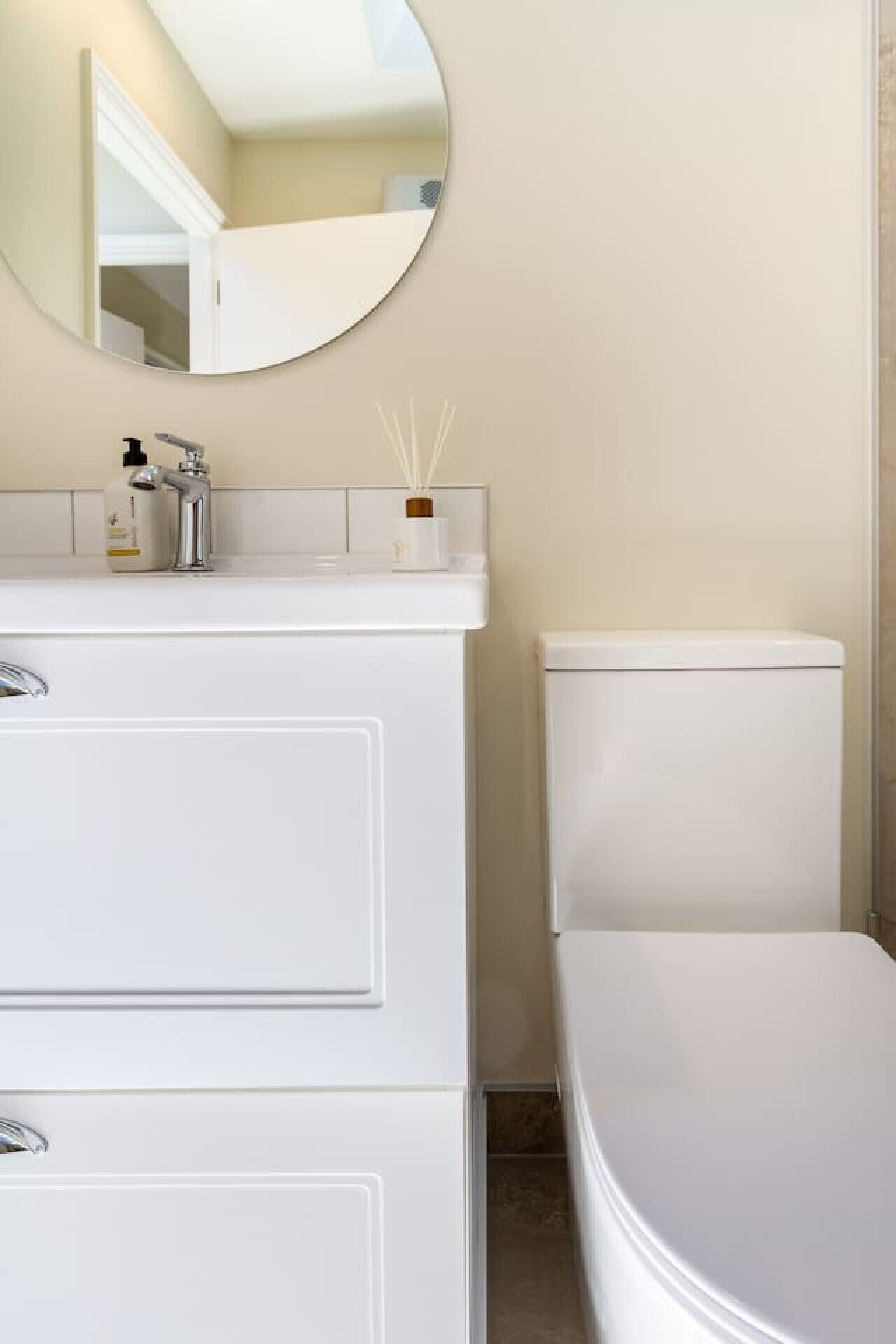 A bathroom with a white vanity, a round mirror, and a toilet.